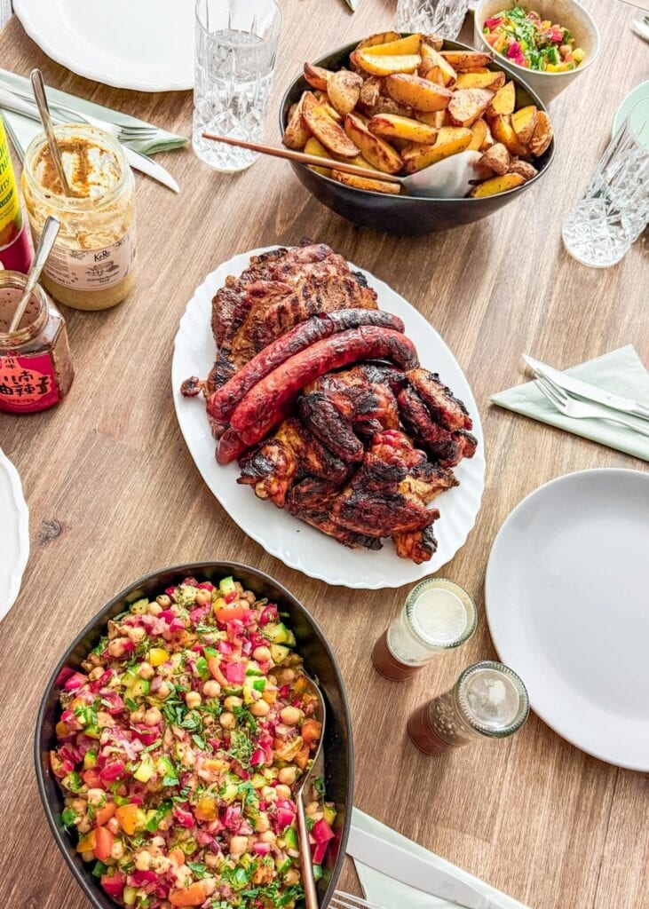 Grillen mit Freunden: Tisch voller Grillgut, Kichererbsensalat und Kartoffelspalten